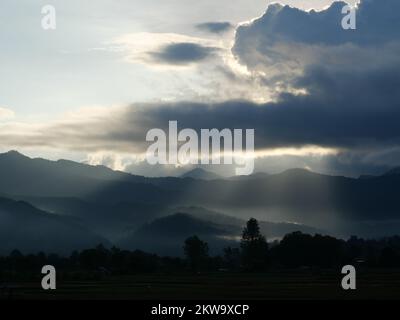 Silhouette d'arbre et de montagne avec la lumière de sunbeam pousse à travers le nuage sombre jusqu'à la terre au lever du soleil, Mist couvre la forêt et les montagnes à l'aube Banque D'Images