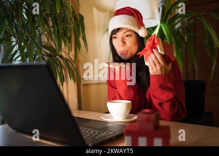 Bonne femme hipster soufflant l'air baiser à son mari tout en faisant le videocall sur ordinateur portable à la maison à la veille de Noël. Copier l'espace Banque D'Images