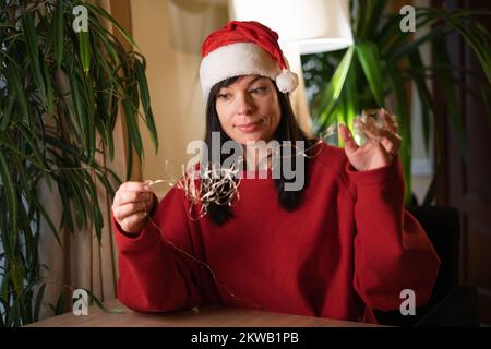 Guirlande emmêlée. Une jeune femme dans un chapeau de père Noël démêle une guirlande le réveillon de Noël. copier l'espace Banque D'Images