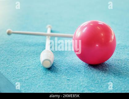 Une boule rouge sur le sol sur un tapis bleu avec club de gymnastique. Appareils de gymnastique, de fitness et d'entraînement pour la gymnastique rythmique isolée sur bleu Banque D'Images