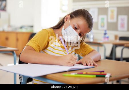 L'école, l'éducation et l'apprentissage avec masque covid sur le visage de fille dans la classe, l'écriture ou la tâche seule. Un système dédié, intelligent et discipliné Banque D'Images