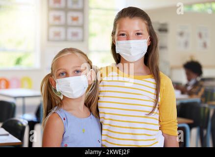 Les jeunes enfants apprennent en classe, après une pandémie de covid, portant des masques ensemble à l'école. Portrait de petites filles élèves, en attente de leur Banque D'Images