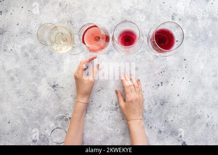 Les mains des femmes choisissent un verre de vin blanc, rose, rouge et bordeaux sur fond de béton. Fond de vin plat Banque D'Images