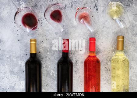 Différentes bouteilles de vin et verres à vin avec bordeaux, rouge, rose et blanc sur fond de béton. Vue de dessus. Papier peint abstrait vin. Banque D'Images