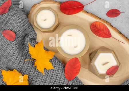 Bougies en pots dorés, feuilles d'automne rouges et jaunes, composition minimale. Le concept de la chaleur et du confort à la maison Banque D'Images