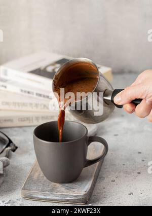 Versez à la main du chocolat chaud dans la tasse pour vous détendre à la maison. Mug avec boisson chaude et livres pour le style Hygge. Banque D'Images