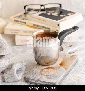 Pot au chocolat chaud sur fond gris en béton avec bougie et livres. Concept de style hygge. Banque D'Images