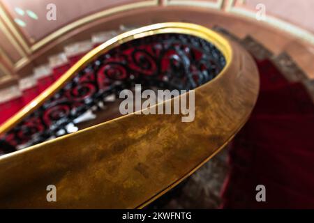 Main courante en laiton d'un escalier en spirale avec tapis rouge. Intérieur classique vintage. Gros plan sur une photo abstraite avec mise au point sélective Banque D'Images