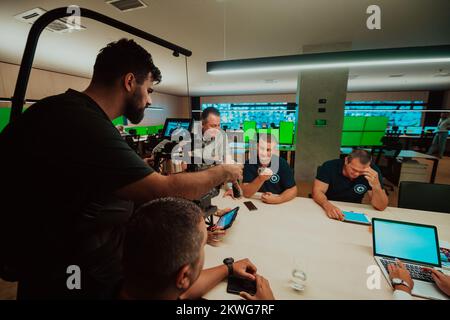 Vidéaste professionnel avec vidéo slr de gimball enregistrant la vidéo des opérateurs de centre de données de sécurité tout en travaillant dans une salle de surveillance de CCTV regardant Banque D'Images