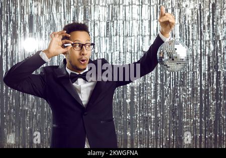 Joyeux bonhomme noir dans un costume s'amusant avec un miroir brillant ballon à une fête disco Banque D'Images