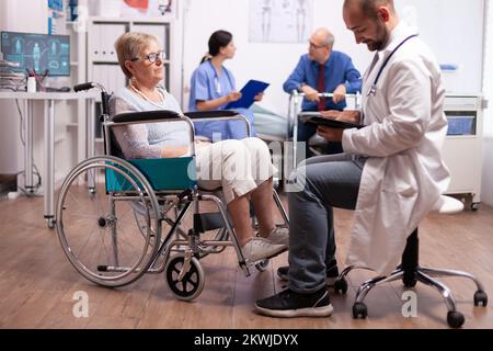 Médecin discutant avec une femme handicapée assise en fauteuil roulant. Homme handicapé, cadre de marche assis dans le lit d'hôpital. Système de soins de santé, patients en clinique. Banque D'Images