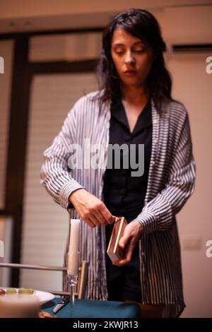 Une femme éclaire la bougie dans la cuisine pour un dîner romantique avec son mari. Femme heureuse caucasienne préparant un repas de fête avec une nourriture saine pour la célébration d'anniversaire, table dans la cuisine. Banque D'Images