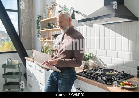 Homme mûr barbu assaisonnement pour une réception dans un livre de cuisine Banque D'Images