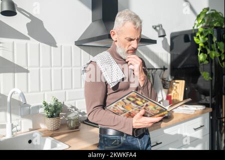 Homme mûr barbu assaisonnement pour une réception dans un livre de cuisine Banque D'Images