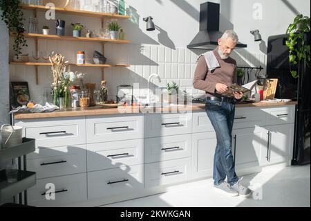 Homme mûr barbu assaisonnement pour une réception dans un livre de cuisine Banque D'Images