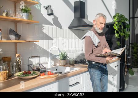 Homme mûr barbu assaisonnement pour une réception dans un livre de cuisine Banque D'Images