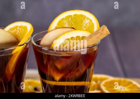 Vin chaud versé dans des tasses en verre placées sur une table en bois, boissons alcoolisées d'hiver décorées de bâtons de cannelle, vue rapprochée Banque D'Images