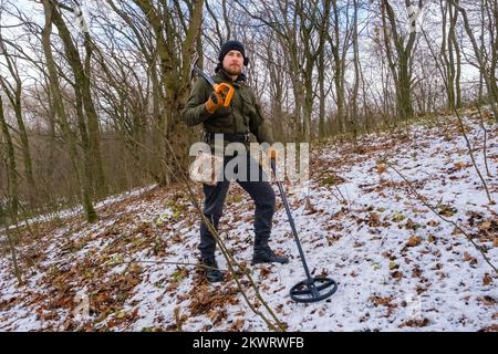 Homme avec détecteur de métaux et pelle dans la forêt enneigée Banque D'Images