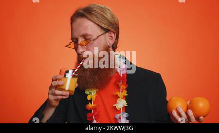 Jeune homme touristique tenant, montrant des fruits oranges, mode de vie végétarien, vitamines pour la santé, vacances heureux, eco-food bio, jus de paille à boire. Jeune garçon sur fond orange Banque D'Images