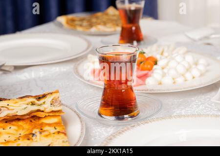 Photo en gros plan du thé turc, table du petit déjeuner. Plat traditionnel du matin. Patty appelée su borek avec de la viande. Assiette de fromages, salami, jambon cru sur le bureau. Banque D'Images