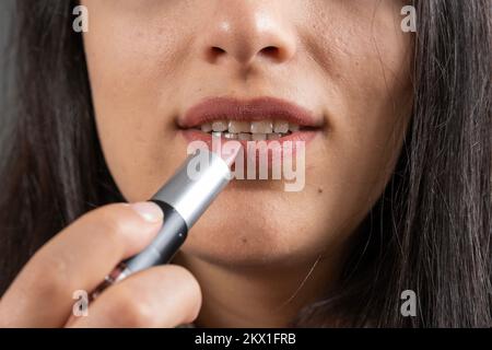 Routant ses lèvres, vue de face de la femme routant ses lèvres. Tenir, utiliser, appliquer le rouge à lèvres rose. Photo d'idée de concept de beauté recadrée. Banque D'Images