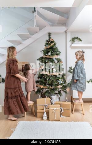 Deux filles avec leur mère décorant l'arbre de noël dans leur salon Banque D'Images