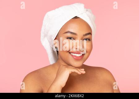 Concept après spa. Portrait d'une femme noire chubby avec serviette de bain sur la tête et peau brillante parfaite souriant à l'appareil photo Banque D'Images