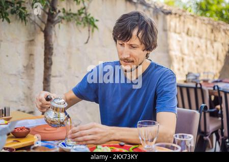 Homme prenant le petit déjeuner turc. Table de petit-déjeuner turc. Pâtisseries, légumes, légumes verts, olives, fromages, oeufs frits, épices, confitures, miel, thé en cuivre Banque D'Images