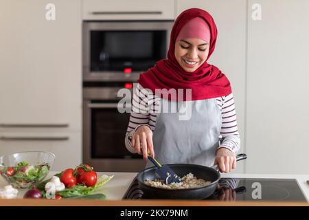 Une jolie jeune femme musulmane en foulard prépare de la nourriture dans la cuisine Banque D'Images