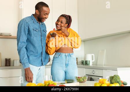 Un jeune mari noir heureux et une femme cuisent le déjeuner ensemble dans la cuisine, un couple aimant faisant de la salade de légumes Banque D'Images