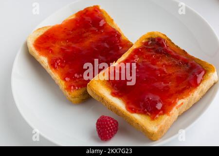 Toasts avec confiture de framboises sur fond blanc Banque D'Images