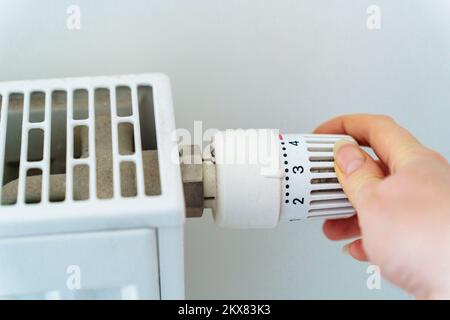 Une main tourne le régulateur sur le radiateur de chauffage de la maison. Le concept d'économie de ressources et d'énergie thermique en relation avec la crise énergétique Banque D'Images