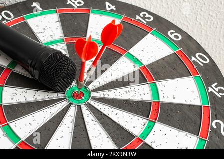 Microphone noir sur un tableau de fléchettes avec 2 fléchettes rouges au milieu de la mise au point en gros plan Banque D'Images