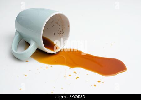 Café renversé d'une tasse bleue sur fond blanc, mise au point douce en gros plan Banque D'Images