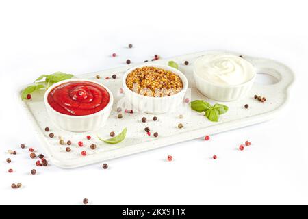 Ensemble de sauces populaires : ketchup, moutarde de dijon et mayonnaise dans de petits bols blancs sur plateau en céramique Banque D'Images