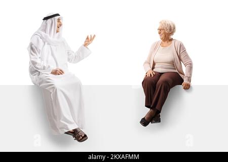 Homme arabe en robe ethnique et femme âgée assise sur un panneau blanc et parlant isolée sur fond blanc Banque D'Images