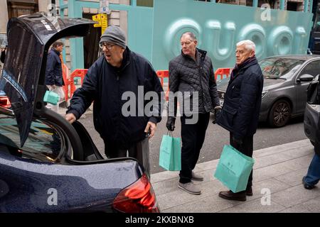 Alors que les ouvriers se préparent à placer un logo Gucci au-dessus de la façade de son nouveau magasin phare sur Bond Street pendant, deux acheteurs masculins tiennent les célèbres sacs verts de Fortnum & Mason, le 29th novembre 2022, à Londres, en Angleterre. Banque D'Images