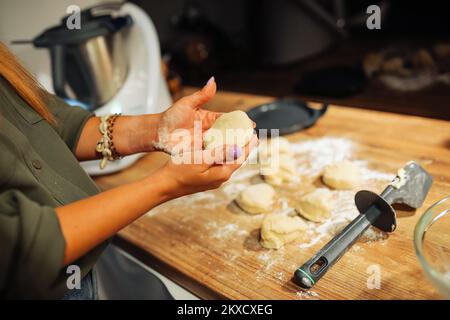 Mains d'une femme tenant un morceau de pâte brute de forme ronde. Couper la pâte en morceaux à l'aide d'un couteau. Dessert maison. Banque D'Images