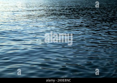 Le détail de la surface calme de la mer avec les petites vagues pendant la soirée alors que le soleil est déjà descendu et les nuances bleues sont venues. Banque D'Images