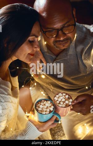 Heureux couple interracial célébrant le nouvel an à la maison ensemble, assis guirlande à proximité l'un de l'autre Banque D'Images