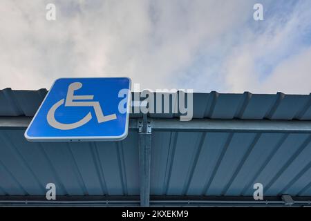 Place de parking gratuite réservée aux personnes handicapées avec le symbole international de handicap peint en blanc sur une plaque en bleu clair sur le dessus du Banque D'Images