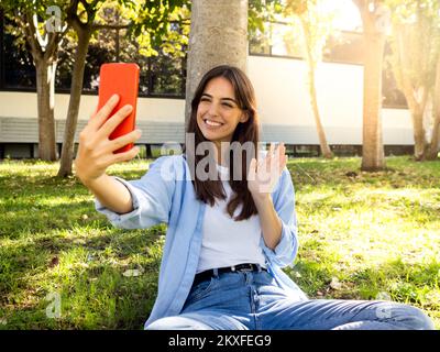 Jeune femme espagnole souriante effectuant un appel vidéo dans un parc avec un smartphone Banque D'Images