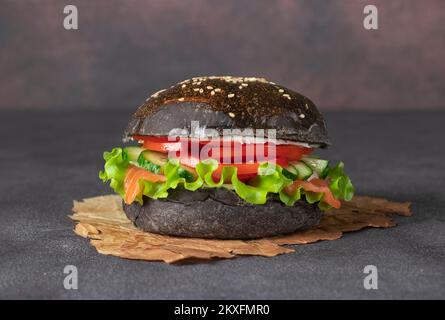 Hamburger noir de légumes avec saumon salé, chair de crabe et légumes sur fond gris Banque D'Images