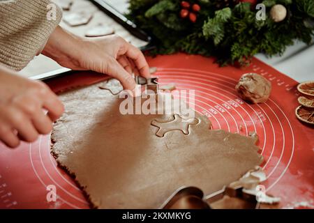 Femme préparant des biscuits de pain d'épice à la cuisine avec des décorations de Noël. Les femmes coupent de la pâte au gingembre avec un couteau pour préparer des biscuits pour les vacances d'hiver Banque D'Images