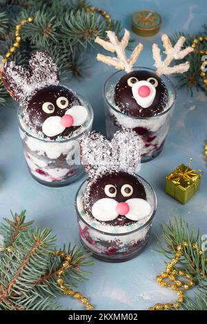 Gâteau en verres sous forme de lapins et de cerfs mignons avec cerises, biscuit au chocolat et flocons de noix de coco sur fond bleu, image verticale Banque D'Images