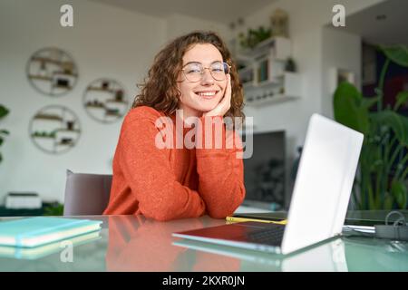 Jeune souriante jolie femme étudiante assise à la table au bureau à domicile avec ordinateur portable. Banque D'Images