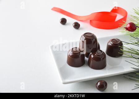 Bonbons au chocolat sur une assiette rectangulaire sur une table blanche et un arc rouge. Vue en hauteur. Banque D'Images