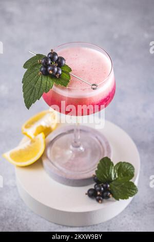 Élégant verre de Black Currant Gin Sour cocktail ou de queues de macktoes entouré d'ingrédients sur la surface de table grise. Boisson rafraîchissante prête à boire. Banque D'Images