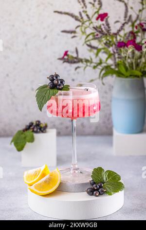 Élégant verre de Black Currant Gin Sour cocktail ou de queues de macktoes entouré d'ingrédients sur la surface de table grise. Boisson rafraîchissante prête à boire. Banque D'Images