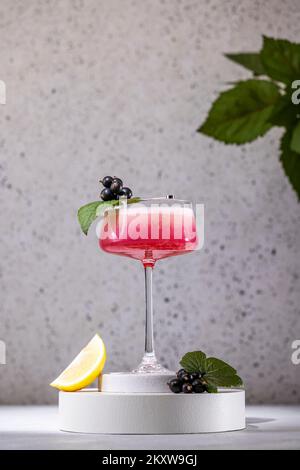 Élégant verre de Black Currant Gin Sour cocktail ou de queues de macktoes entouré d'ingrédients sur la surface de table grise. Boisson rafraîchissante prête à boire. Banque D'Images